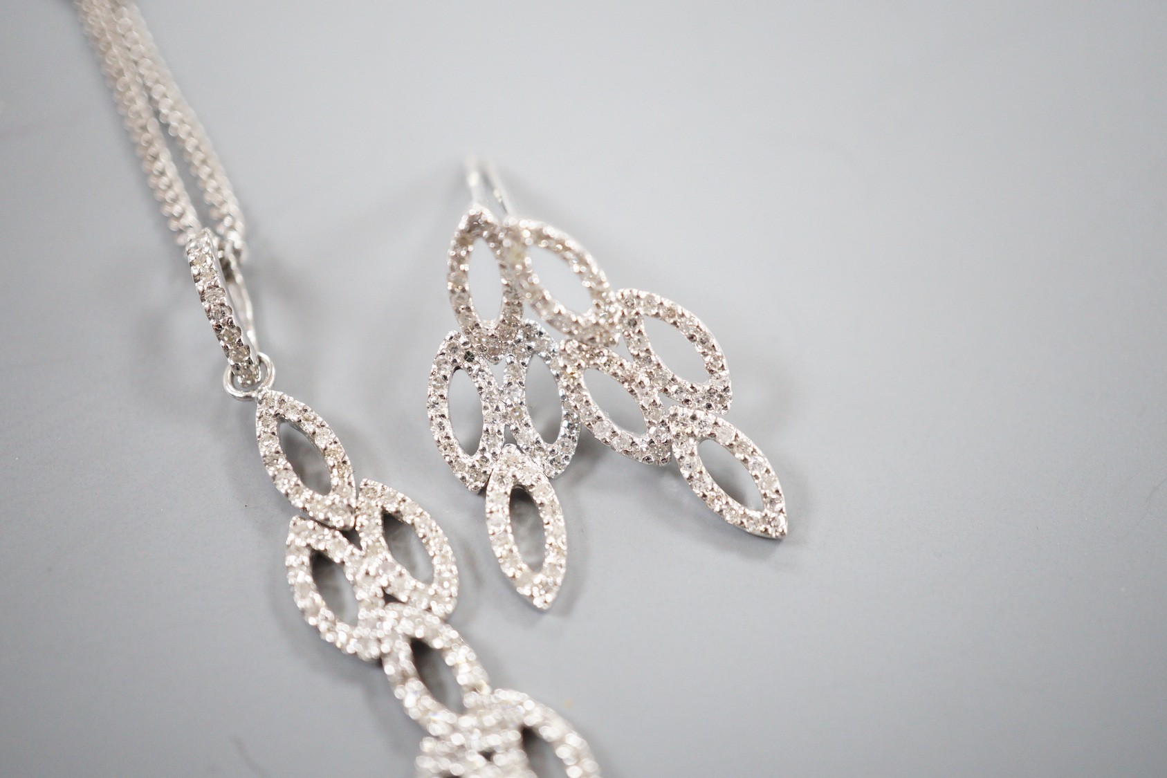 A modern 18ct white gold and diamond chip set septuple oval cluster pendant, overall 42mm, on an 18ct white gold fine link chain, 39cm and a pair of matching earrings, 21mm, gross weight 7.4 grams.